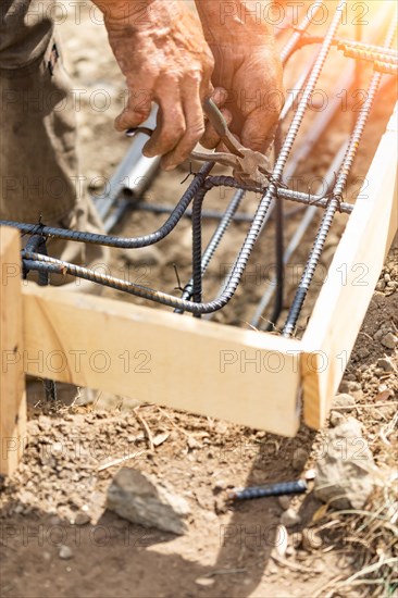 Worker securing steel rebar framing with wire plier cutter tool at construction site