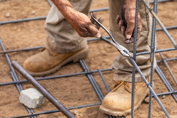 Worker securing steel rebar framing with wire plier cutter tool at construction site