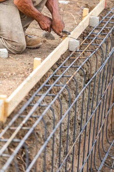 Worker securing steel rebar framing with wire plier cutter tool at construction site