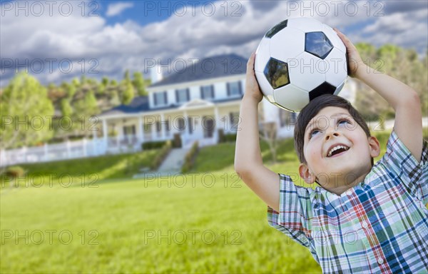 Cute smiling young boy holding soccer ball in front of beautiful house