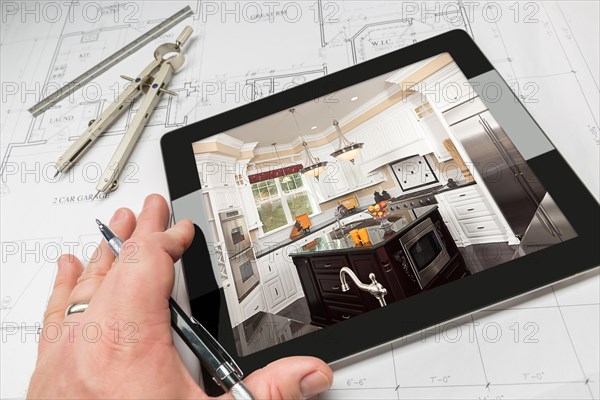 Hand of architect on computer tablet showing custom kitchen photo over house plans