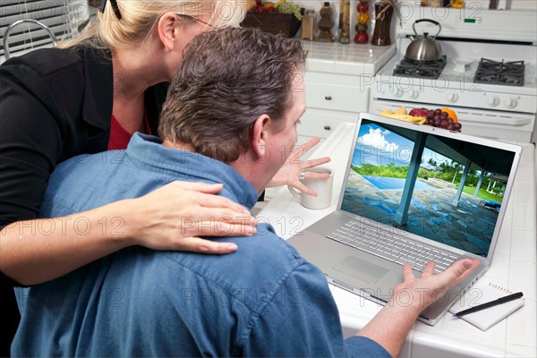Couple in kitchen using laptop to research travel and vacations. screen can be easily used for your own message or picture. picture on screen is my copyright as well