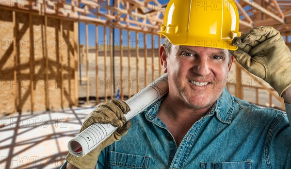 Smiling contractor in hard hat holding floor plans at construction site