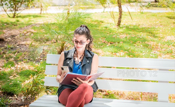 A girl sitting taking notes with a notebook and cell phone