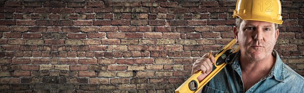 Male contractor in hard hat holding level in front of old brick wall banner with copy space