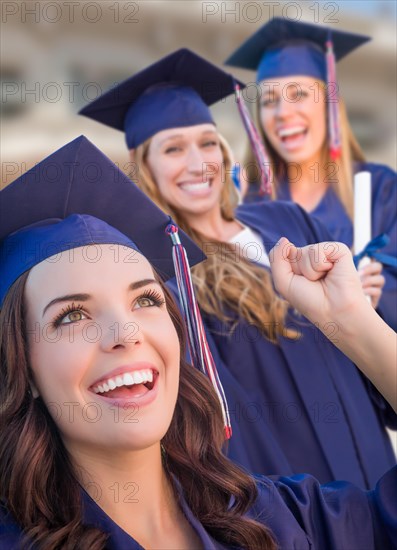 Happy graduating group of girls in cap and gown celebrating on campus