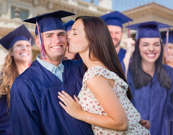 Proud male graduate in cap and gown with girl among other graduates behind