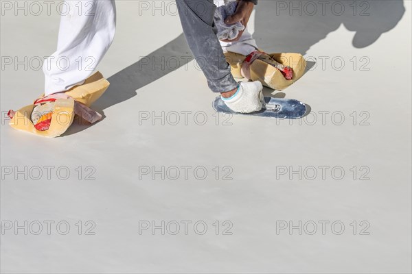Worker wearing sponges on shoes smoothing wet pool plaster with trowel