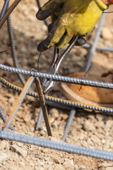 Worker securing steel rebar framing with wire plier cutter tool at construction site