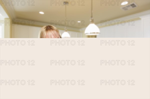 Happy young woman holding blank sign and keys inside beautiful custom kitchen