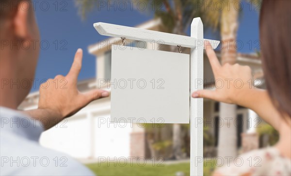 Young military couple framing their hands around blank real estate sign and house