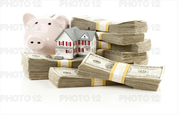 Small house and piggy bank with stacks of hundred dollar bills isolated on a white background