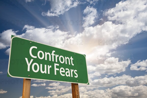 Confront your fears green road sign with dramatic clouds and sky