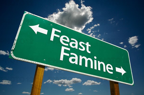 Feast or famine green road sign with dramatic clouds and sky