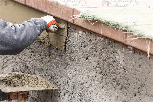 Tile worker applying cement with trowel at pool construction site