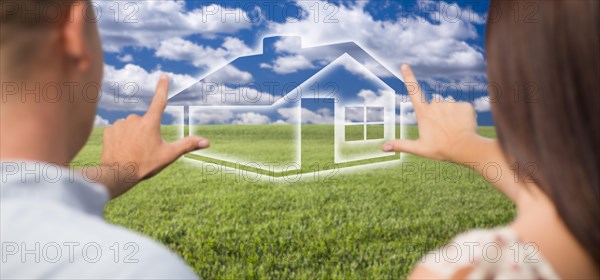 Dreaming couple framing hands around ghosted house figure in grass field