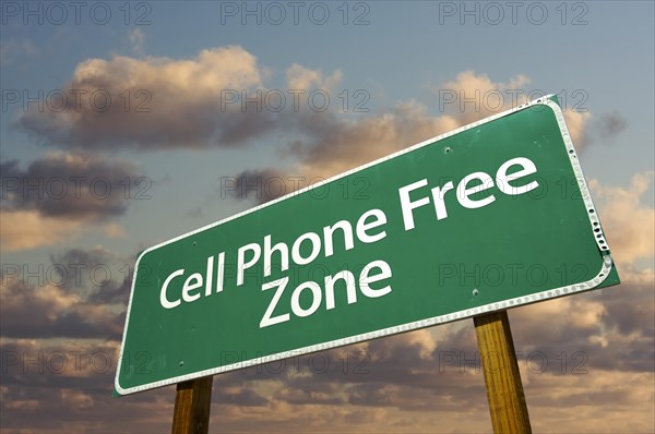 Cell phone free zone green road sign in front of dramatic clouds and sky