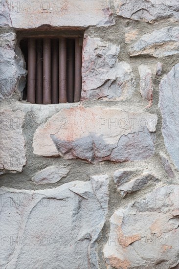 Old stone wall with small iron barred prison cell window