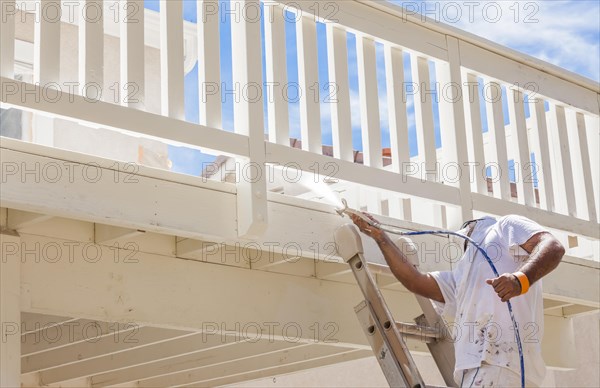 House painter wearing facial protection spray painting A deck of A home