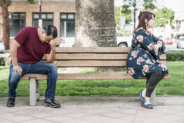 Unhappy mixed-race couple sitting facing away from each other on park bench