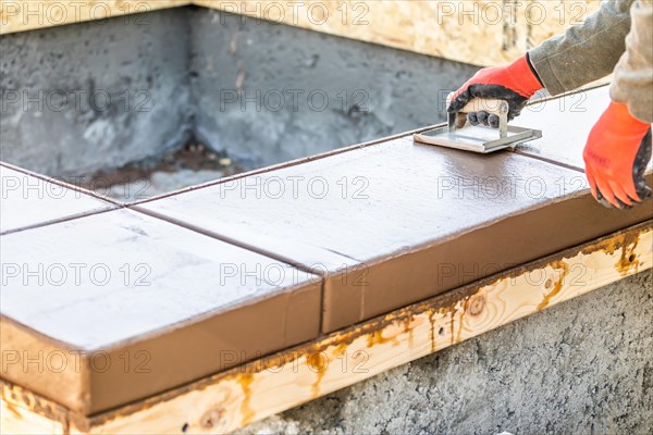 Construction worker using hand groover on wet cement forming coping around new pool