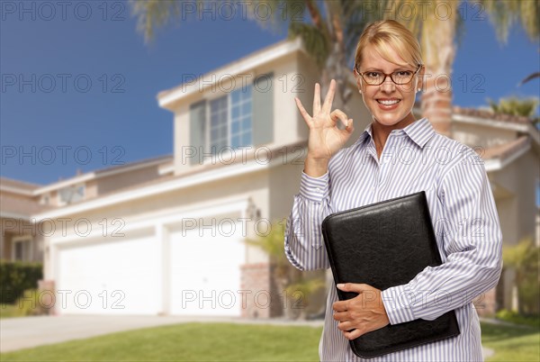 Attractive businesswoman with okay hand sign in front of nice residential home