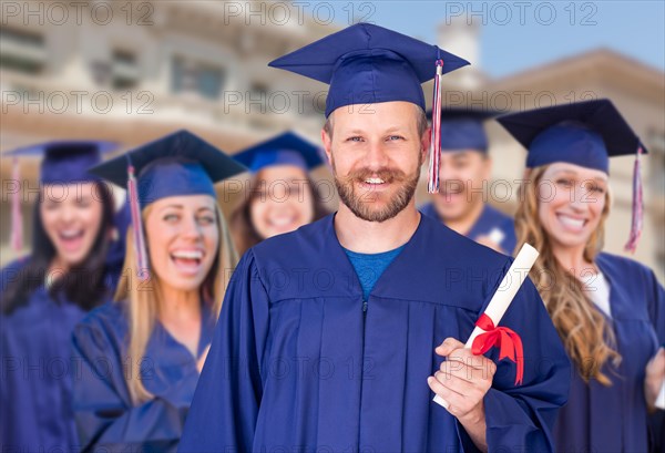 Proud male graduate in cap and gown in front of other graduates