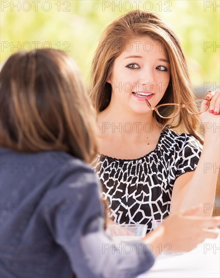 Two mixed-race girlfriends talking over drinks outdoors