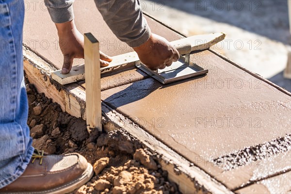 Construction worker using hand groover on wet cement forming coping around new pool