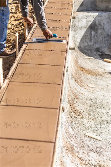 Construction worker using trowel on wet cement forming coping around new pool