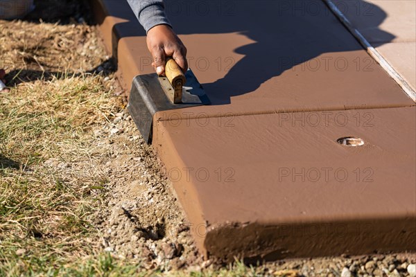 Construction worker smoothing wet cement with curb tool