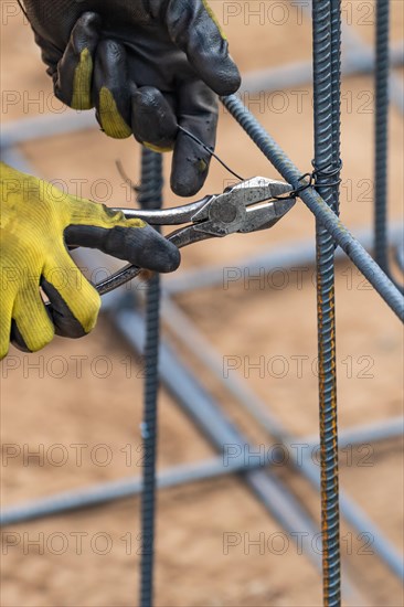 Worker securing steel rebar framing with wire plier cutter tool at construction site