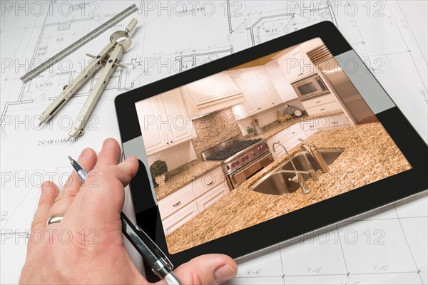 Hand of architect on computer tablet showing custom kitchen photo over house plans