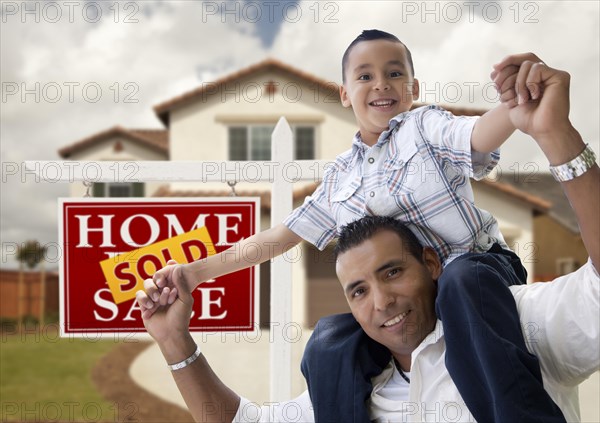 Happy hispanic father and son in front of new house and sold real estate sign