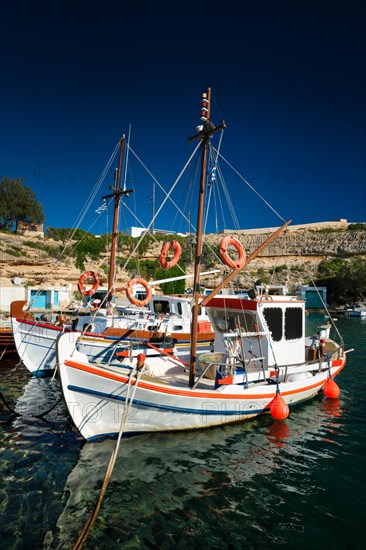 Fishing boats moored in crystal clear turquoise sea water in harbour in Greek fishing village of Mandrakia