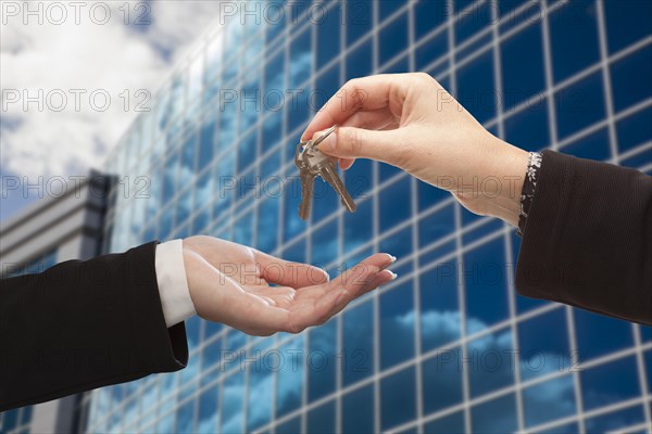 Female handing over the keys to other woman in front of corporate building