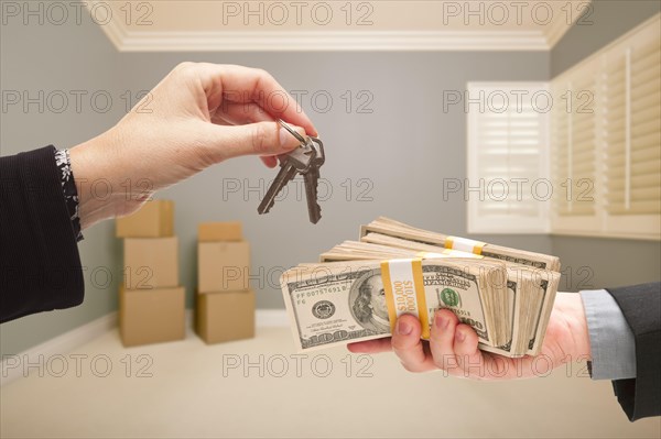 Man and woman handing over cash for house keys inside empty gray room with boxes