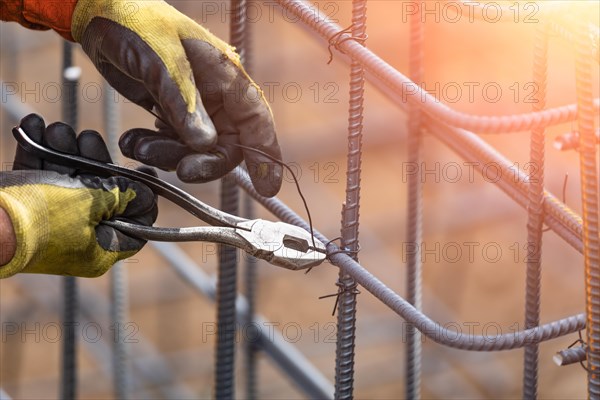 Worker securing steel rebar framing with wire plier cutter tool at construction site