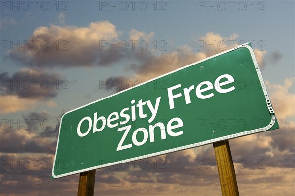 Obesity free zone green road sign in front of dramatic clouds and sky