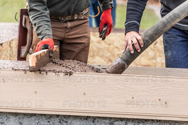 Construction workers pouring and leveling wet cement into wood framing