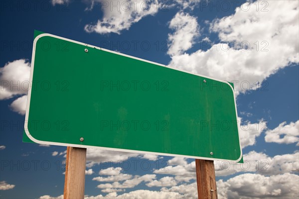 Blank green road sign on dramatic blue sky with clouds