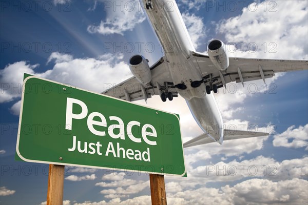 Peace green road sign and airplane above with dramatic blue sky and clouds