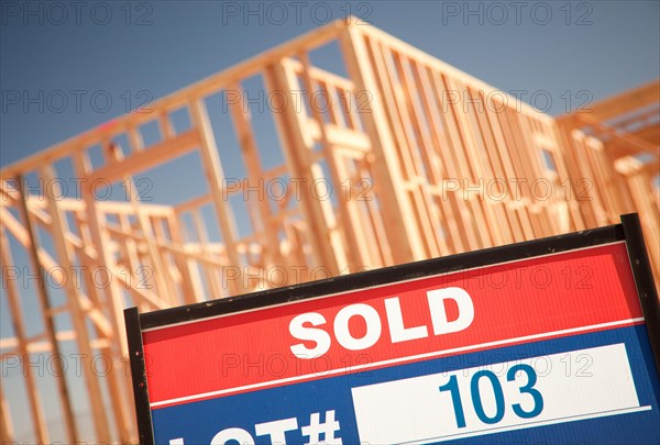 Sold lot real estate sign at new home framing construction site against deep blue sky