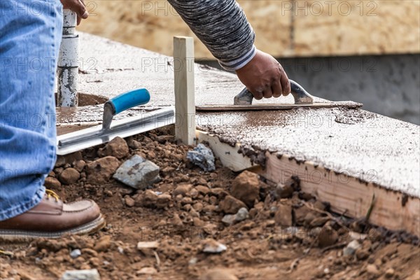 Construction worker using wood trowel on wet cement forming coping around new pool