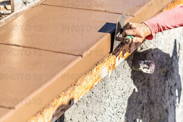 Construction worker using stainless steel edger on wet cement forming coping around new pool