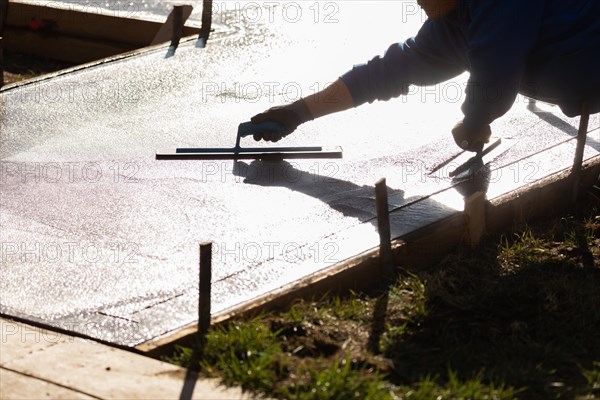 Construction worker smoothing wet cement with trowel tools