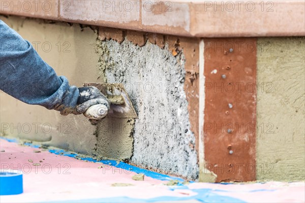 Tile worker applying cement with trowel at pool construction site