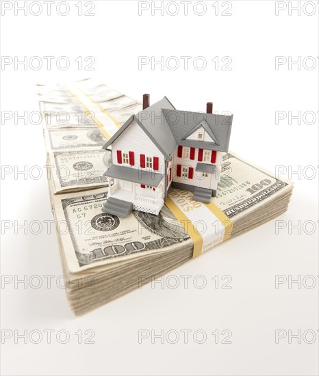 Small house on row of hundred dollar bill stacks isolated on a white background