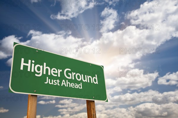 Higher ground green road sign against dramatic sky