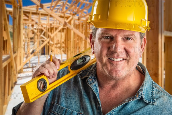 Smiling contractor in hard hat holding level and pencil at construction site
